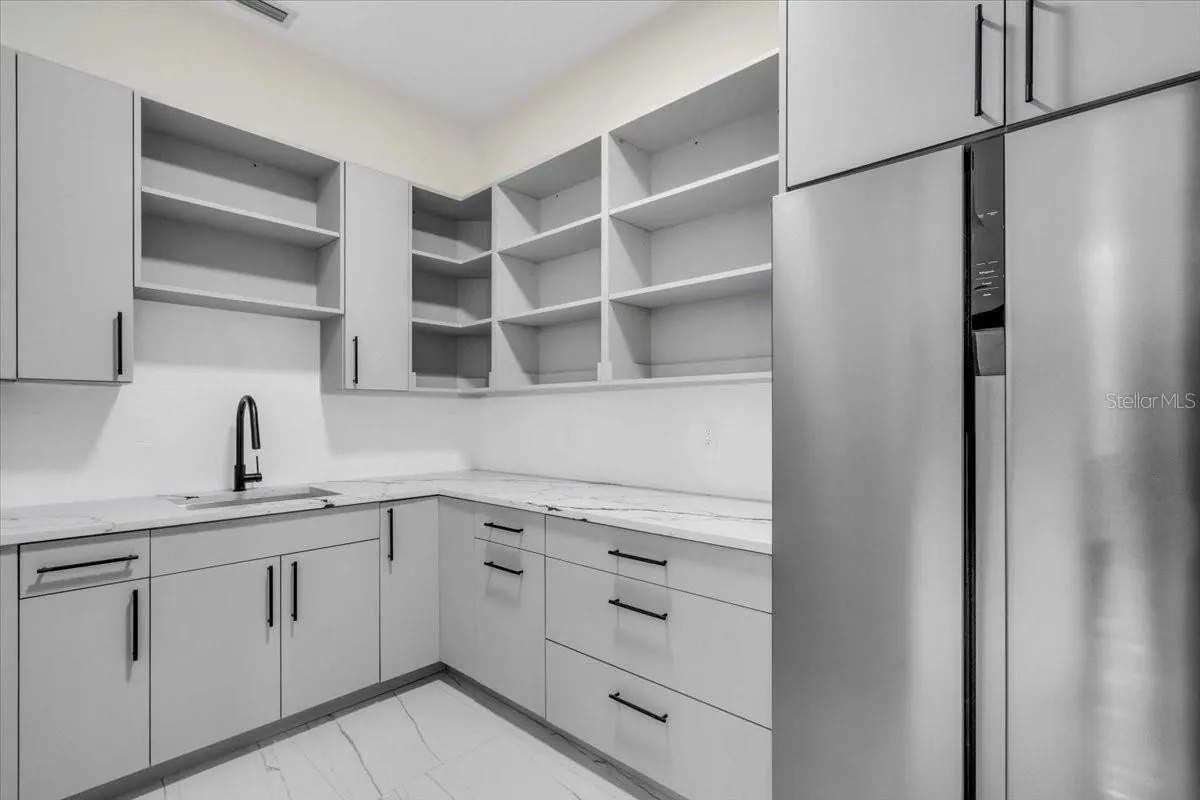 Butler's pantry with open shelving, quartz counters, and a stainless-steel refrigerator.