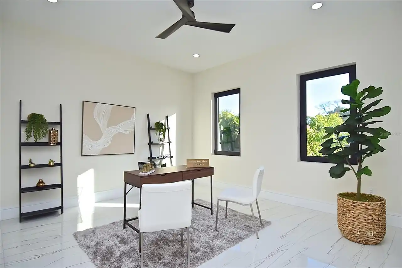 Home office with a wood desk, ladder shelving, and a potted fiddle-leaf fig by the window.