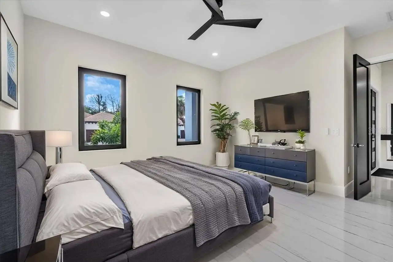 Bedroom staged with a gray upholstered bed, blue dresser, and wall-mounted TV.