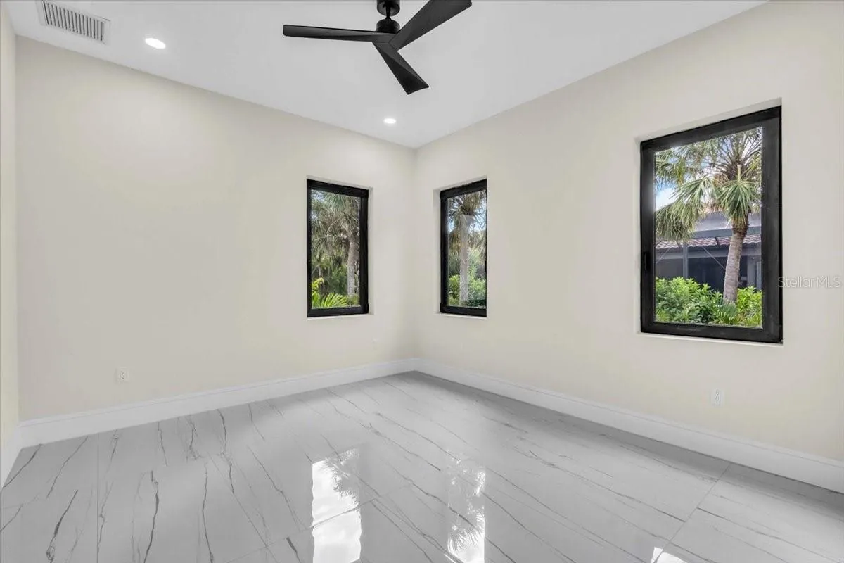 Unfurnished bedroom with a bank of three windows overlooking mature palms.