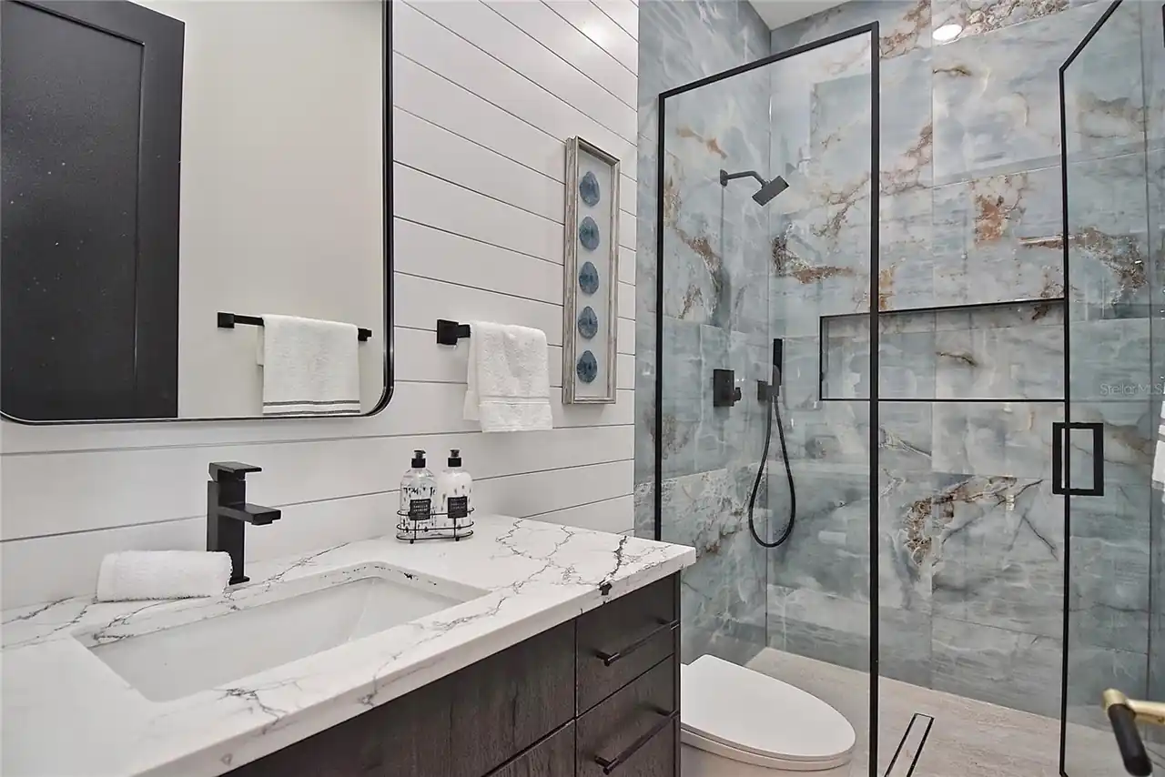 Bathroom with shiplap walls and a glass-enclosed shower finished in blue-veined marble.