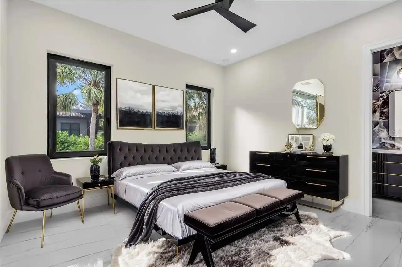 Primary bedroom with a charcoal tufted bed, gold-framed mirror, and palm-tree views.