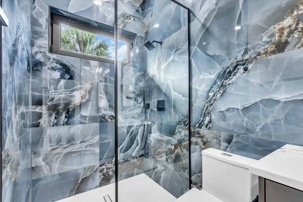 Walk-in shower finished in dramatic blue-and-gold marble slab with a small window.