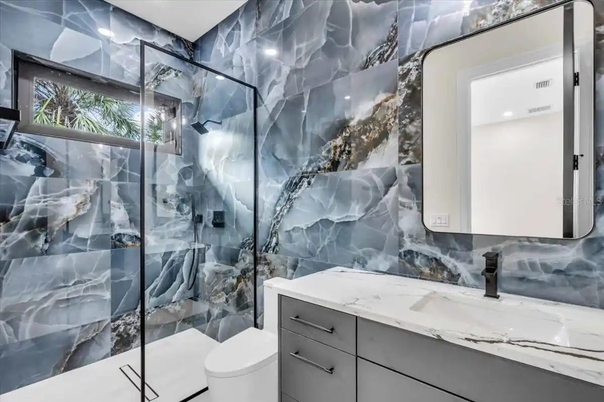 Bathroom combining a marble slab shower with a gray vanity and wall mirror.