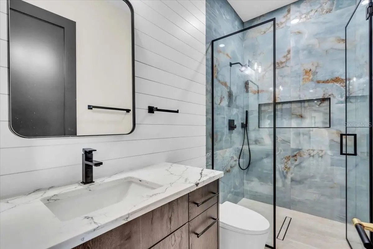 Vanity with a marble countertop beside a glass shower enclosed in matching stone.