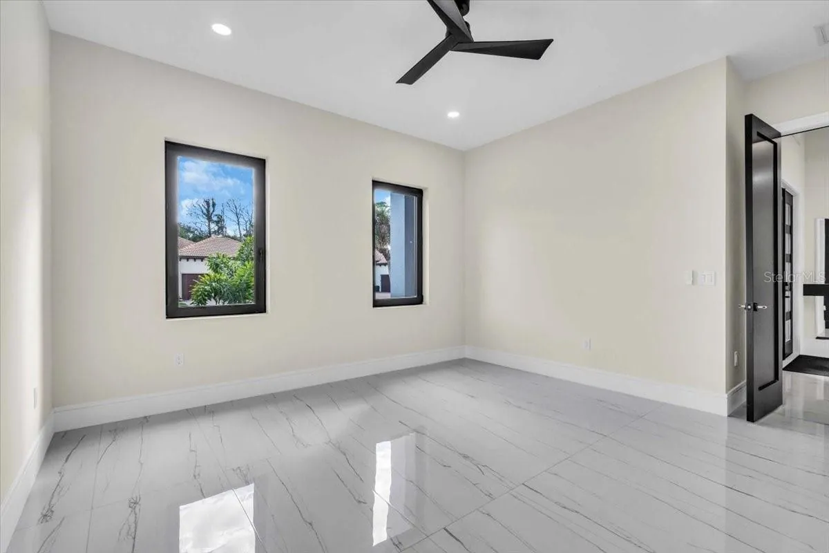 Empty bedroom with corner windows and a dark wood door leading to the hallway.