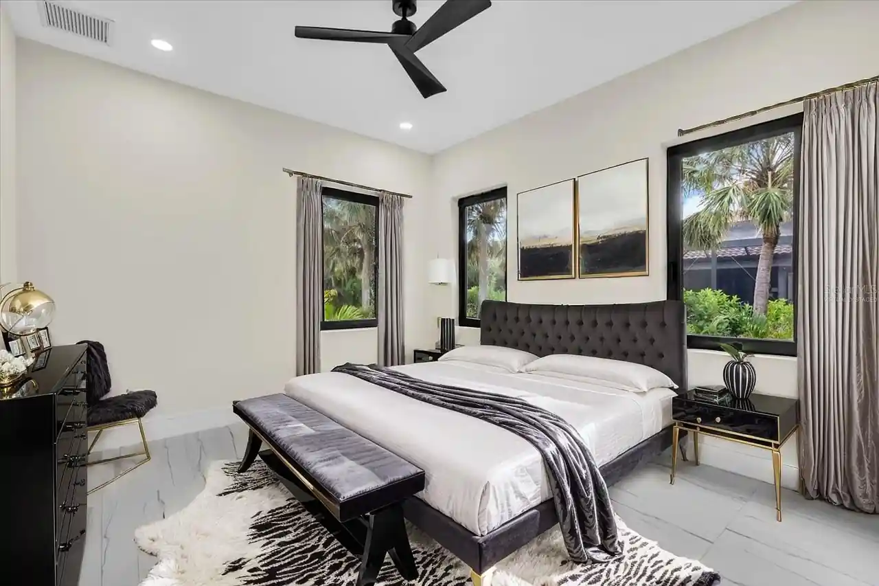 Primary bedroom with a tufted headboard, gold-trimmed nightstands, and curtained palm views.