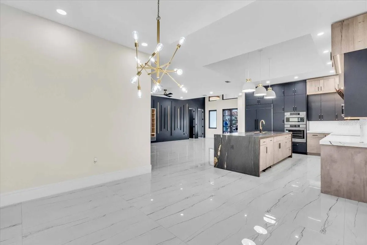 Open kitchen and living space with a marble waterfall island and brass chandelier.