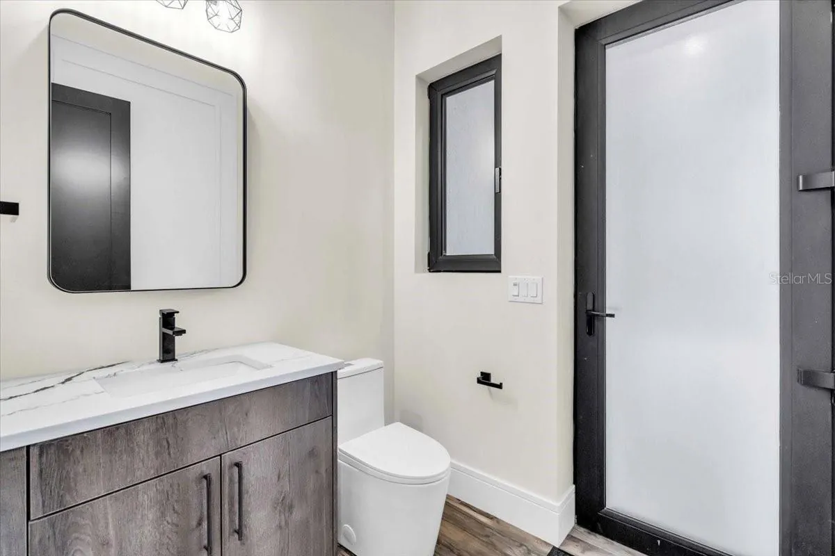 Powder bathroom with a round mirror, black fixtures, and a frosted glass door.