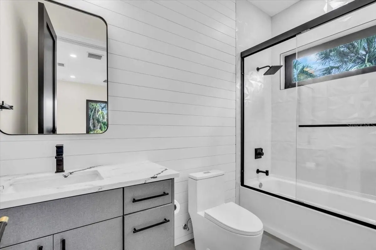 Bathroom with shiplap walls, a black-framed mirror, and a tub-shower combo.