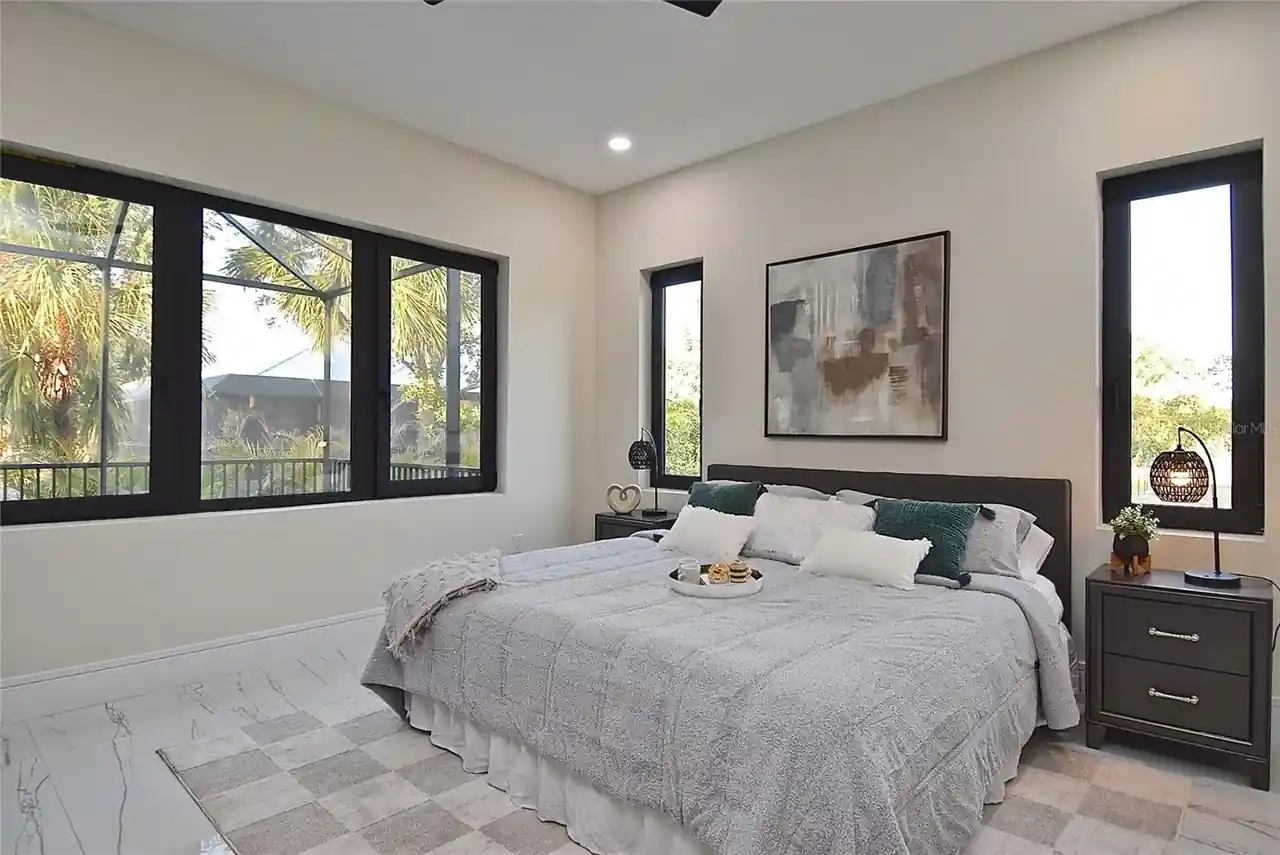 Primary bedroom with a black tufted headboard, teal accent pillows, and lanai-facing windows.