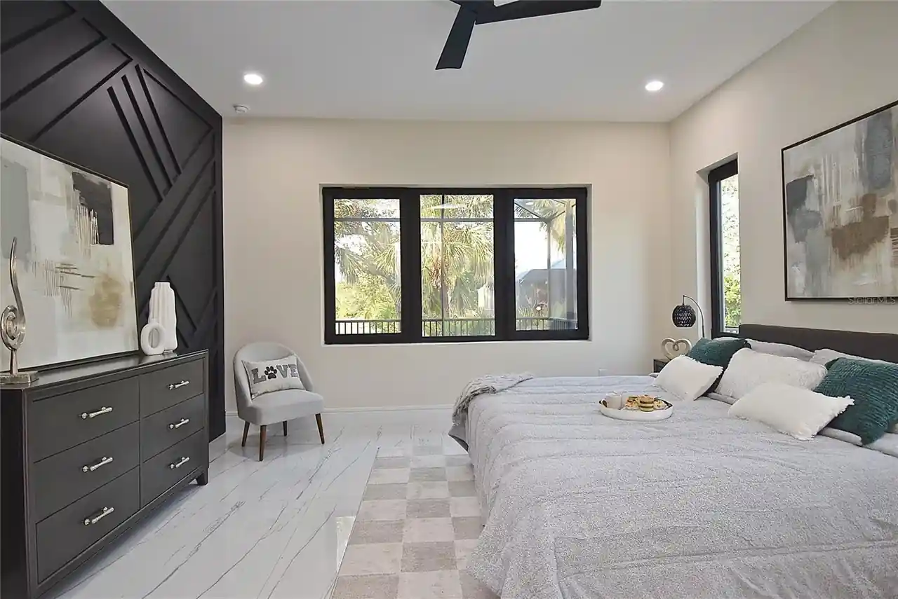 Bedroom with a black geometric accent wall, dark dresser, and a triple window overlooking the lanai.