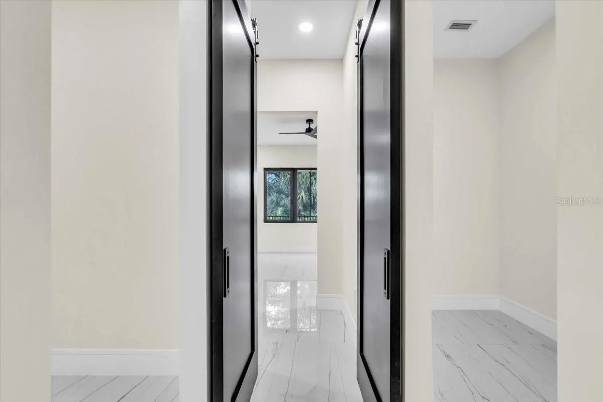 Hallway with black sliding barn doors opening toward a sunlit bedroom.