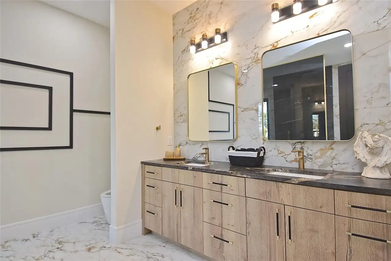 Primary bath double vanity with a marble slab backsplash and gold fixtures.