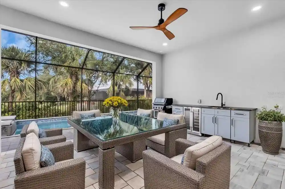 Covered lanai with a wicker dining set overlooking the pool and outdoor kitchen.