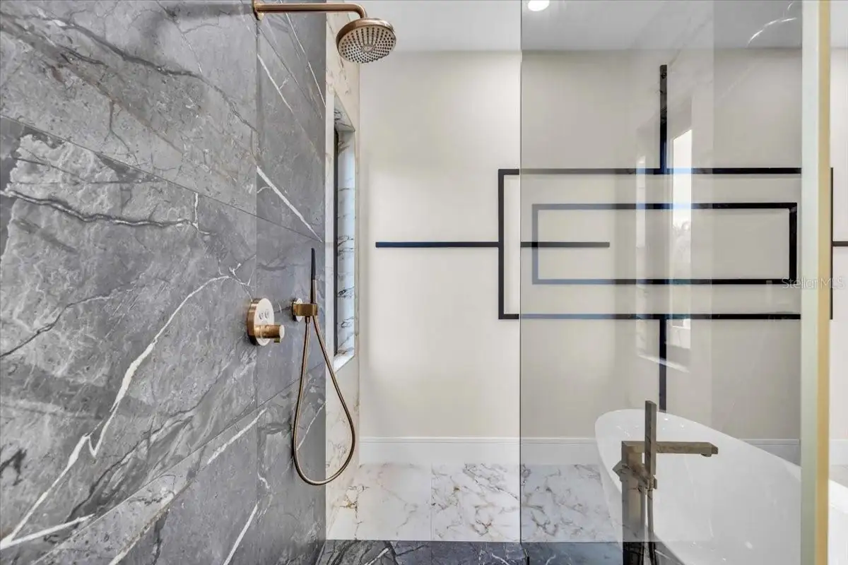 Close-up of a gold rainfall shower head and handheld sprayer against stone tile.