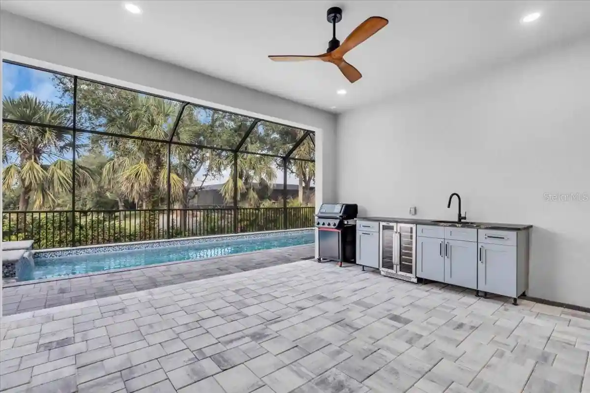 Outdoor kitchen with a grill and beverage cooler beside the screened pool deck.