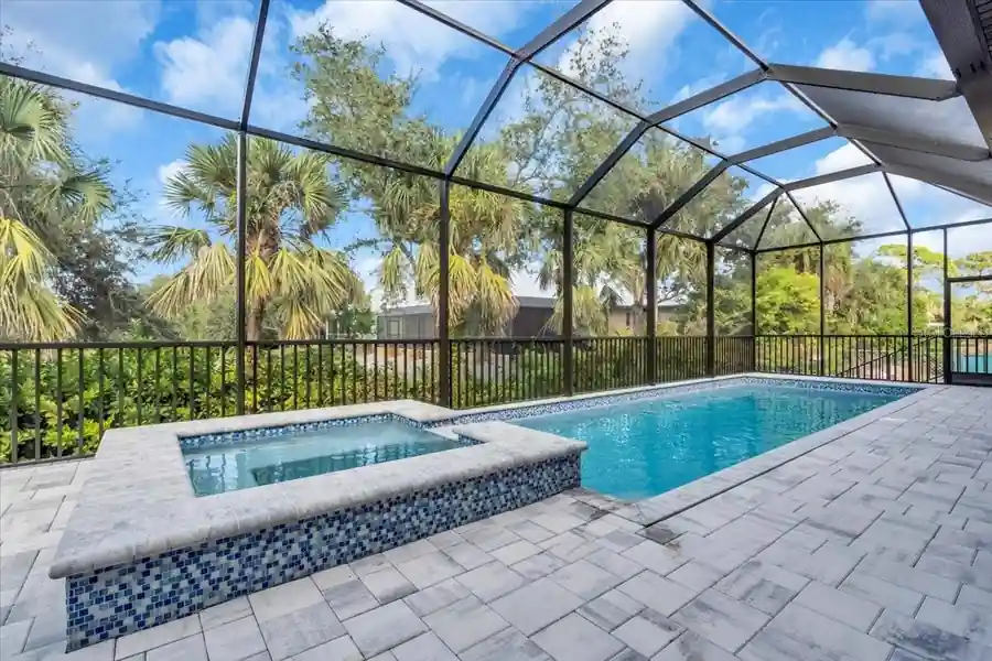 Elevated spa spilling into the pool within a screened lanai enclosure.