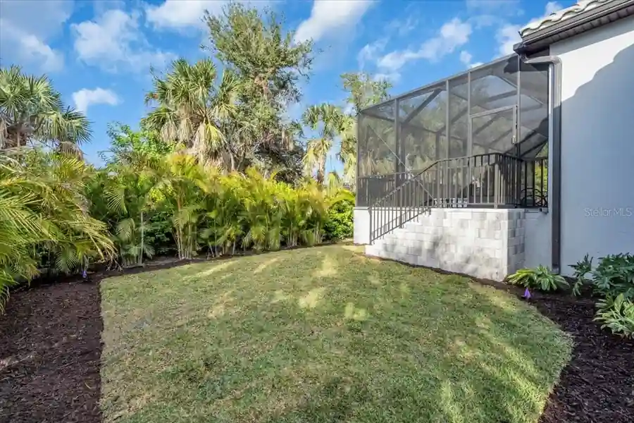 Backyard lawn framed by mature palms, with stairs leading up to the screened lanai.