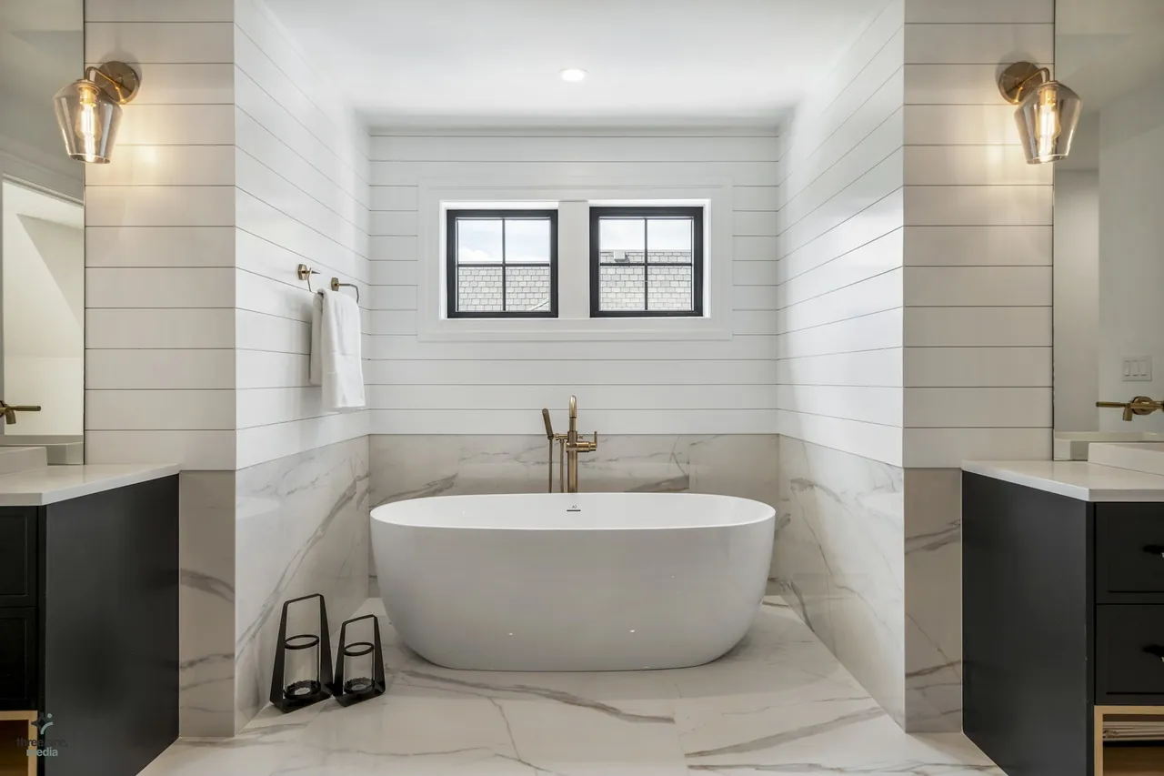 Primary bath tub alcove framed in marble slab with brass fixtures