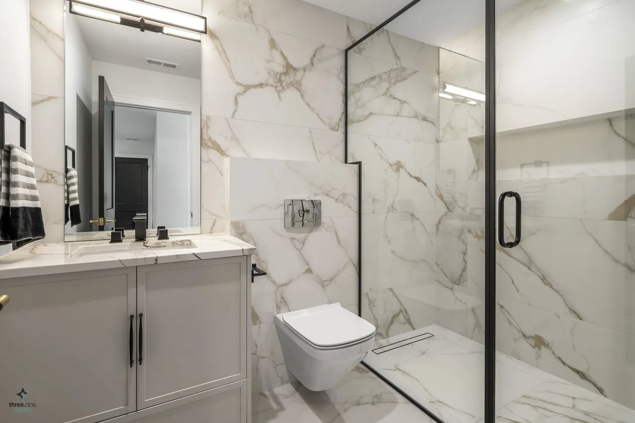 Bathroom with a wall-mounted toilet and marble-tiled glass shower enclosure