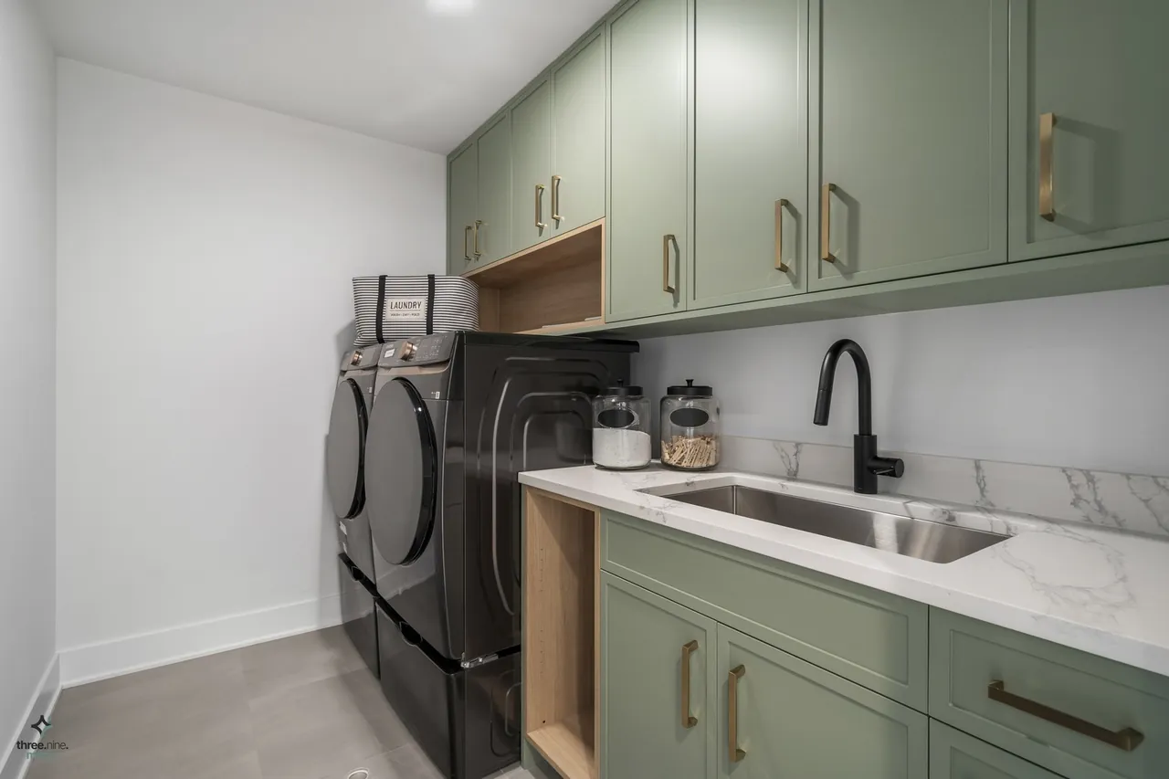 Laundry room with sage green cabinetry and a marble backsplash