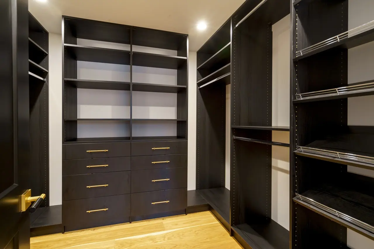 Walk-in closet with dark wood built-ins and brass drawer pulls