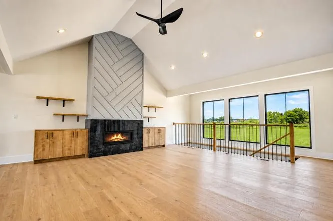 Great room overlooking the open loft railing, wood floors, and windows facing the backyard lawn.