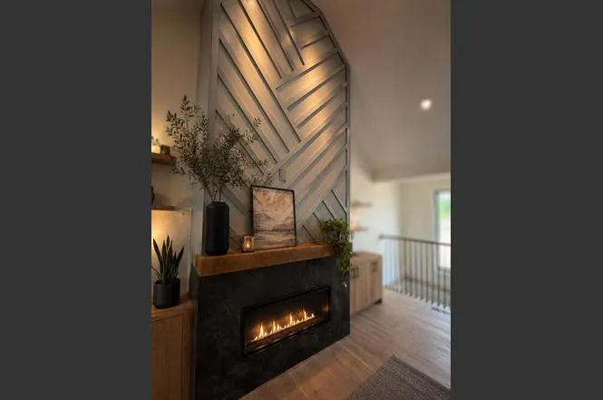 Close-up of the great room fireplace with herringbone tile surround, wood mantle, and decorative floating shelves.