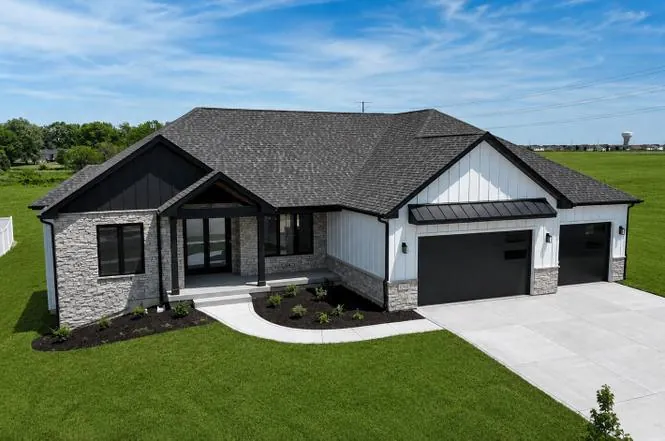 Daytime aerial-angle exterior of the ranch home with stone accents, white board-and-batten siding, and a dark three-car garage.