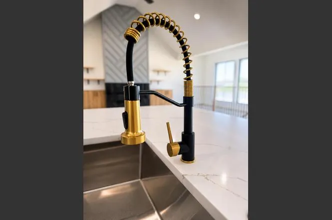 Detail shot of the kitchen's matte black and brushed gold gooseneck faucet over a stainless steel sink.