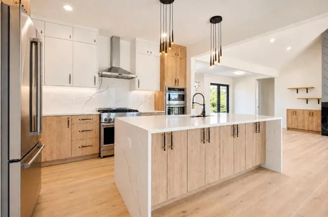 Kitchen view toward the range hood and wall ovens, with wood cabinetry and a quartz waterfall island.