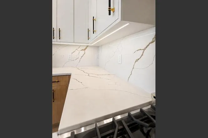 Close-up of the waterfall quartz countertop and marble-look backsplash behind the gas cooktop.