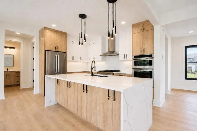 Kitchen with white and natural wood cabinetry, a waterfall quartz island, and a stainless steel refrigerator.