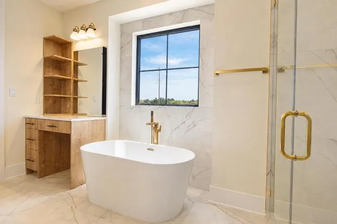 Primary bathroom featuring a freestanding soaking tub, brass floor-mount filler, and marble tile surround.