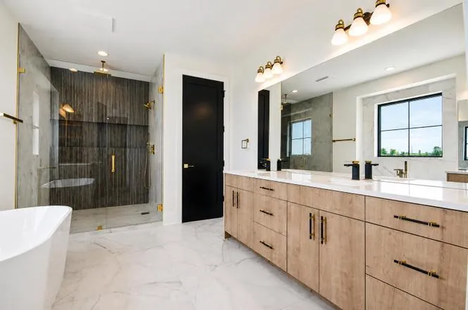 Primary bathroom with a glass-enclosed shower, dark linear tile, brass fixtures, and a wood double vanity.