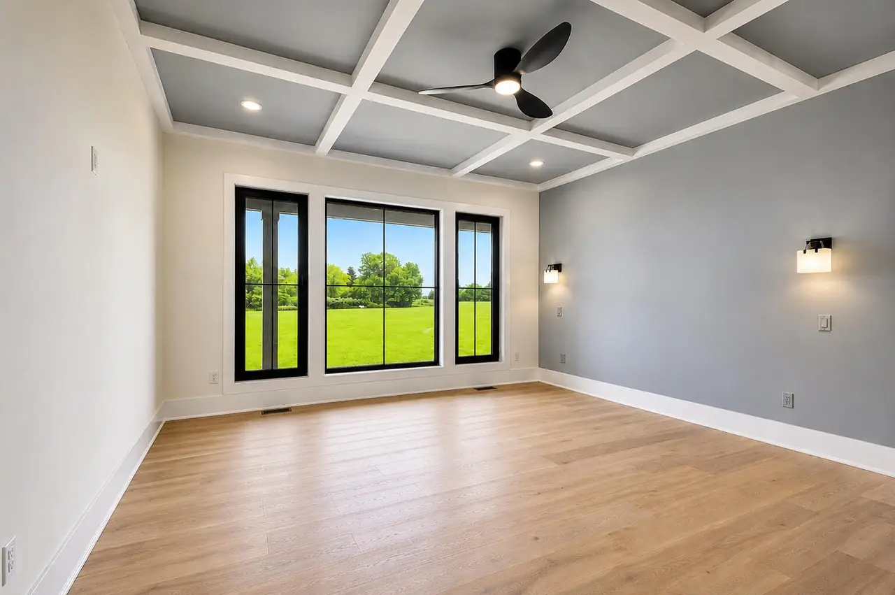 Bonus room with a gray coffered ceiling, ceiling fan, and a large black-framed window overlooking the yard.