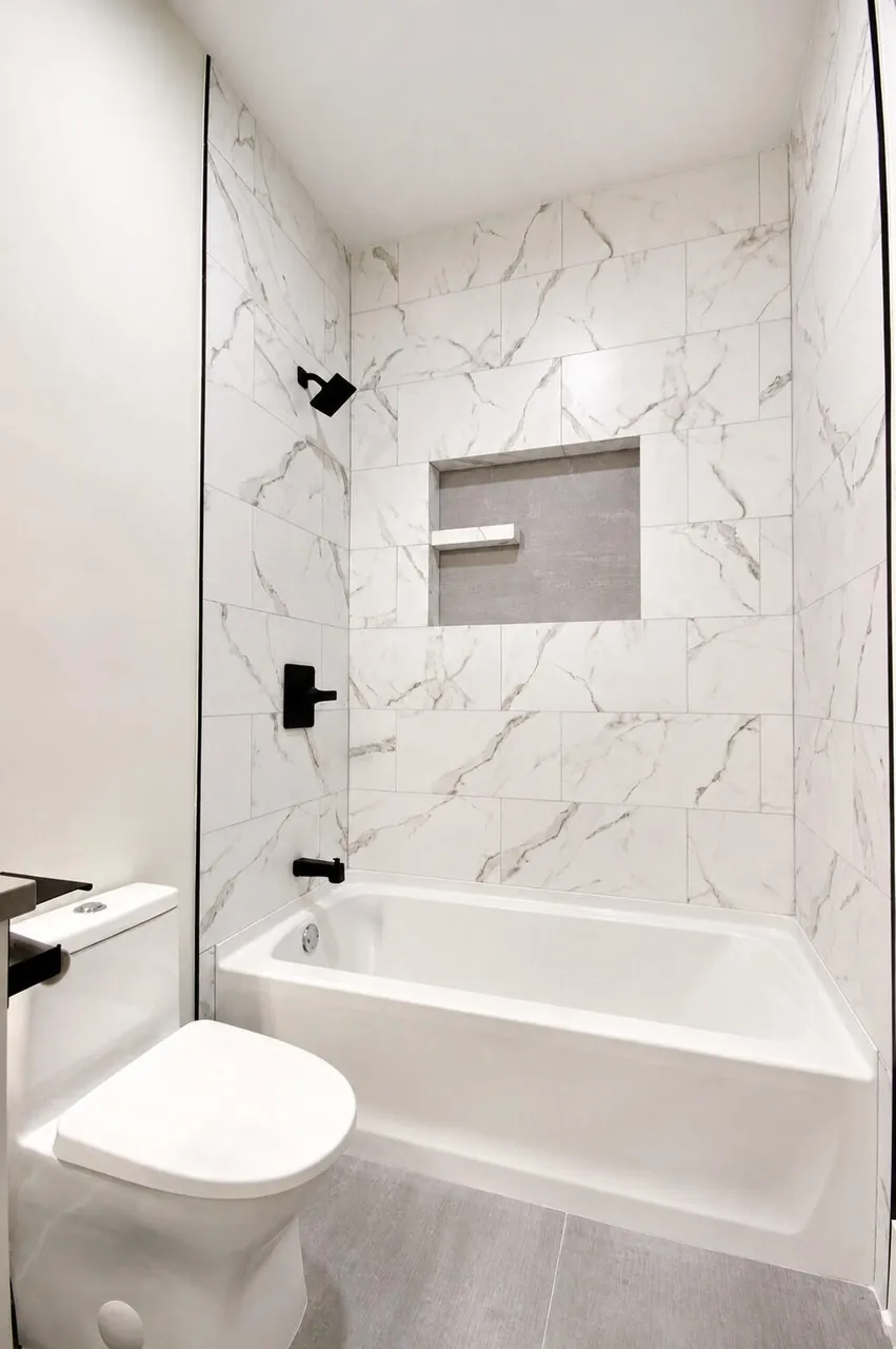 Tub-shower combo with marble subway tile surround, a built-in niche, and matte black fixtures.