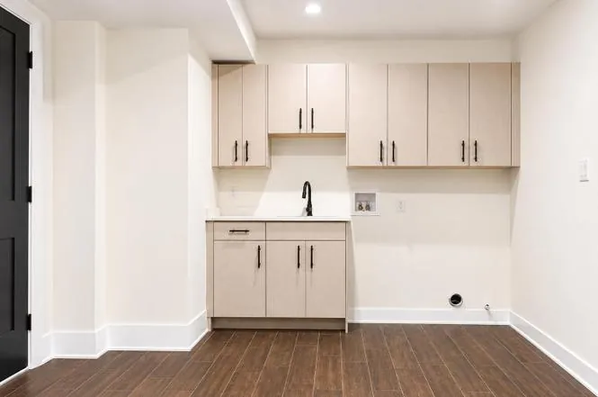 Small laundry or wet bar nook with upper and lower cabinetry and a single basin sink.
