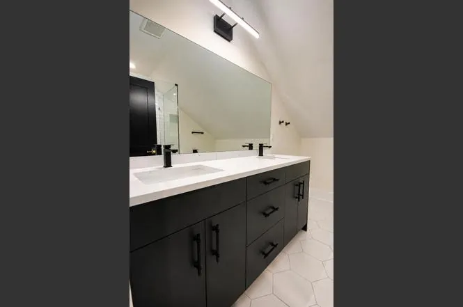 Upper-level bathroom with dark vanity cabinetry, dual sinks, and hexagon tile flooring beneath a sloped ceiling.
