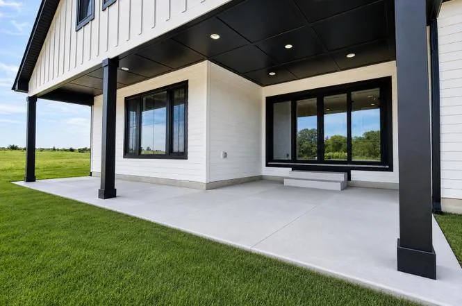 Covered rear patio with black support posts, black ceiling, and white siding overlooking the backyard.