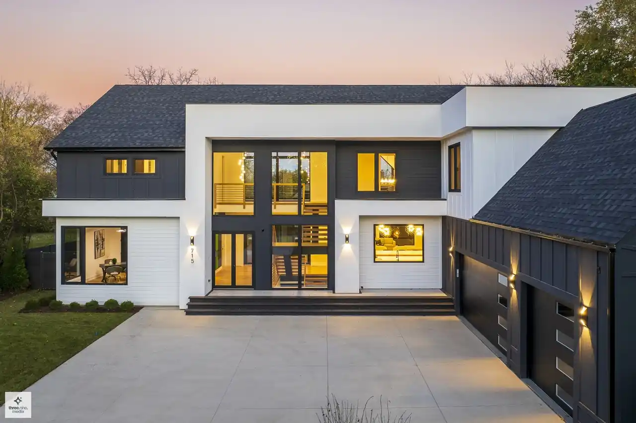 Dusk exterior close-up showing glowing floor-to-ceiling windows and board-and-batten siding