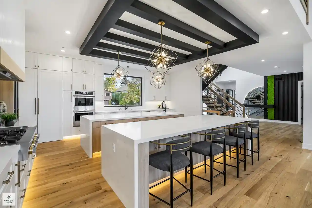 Open-concept kitchen with dual waterfall islands and geometric cube chandeliers under a black beam ceiling