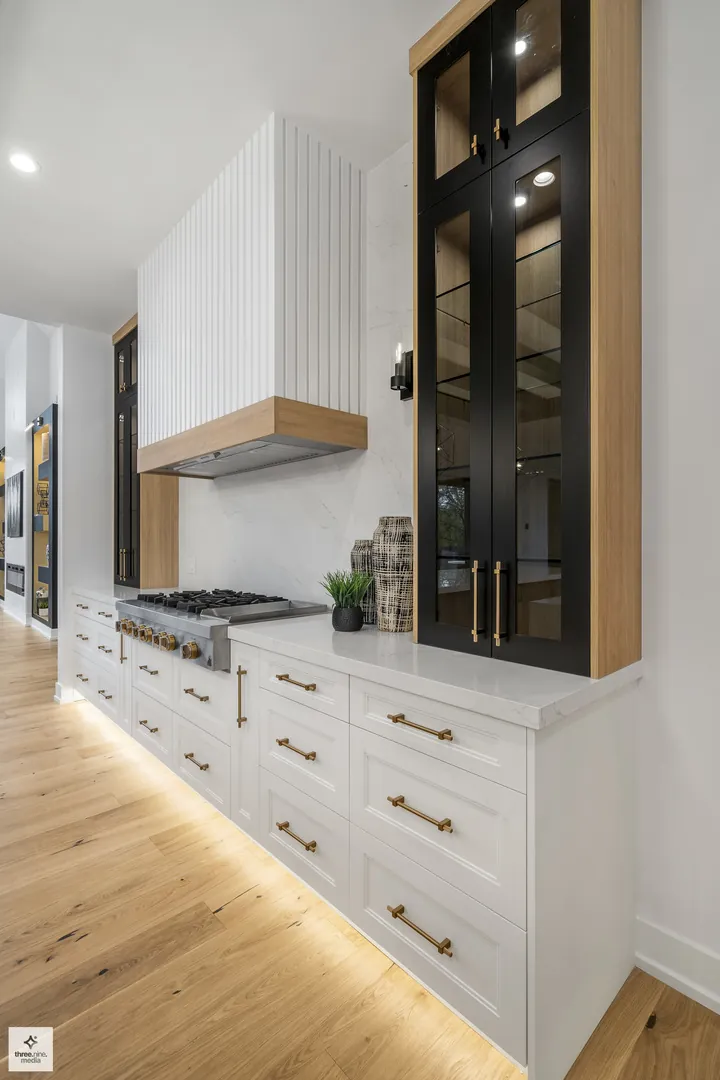 Range and hood detail with fluted paneling and glass-front cabinetry with brass pulls
