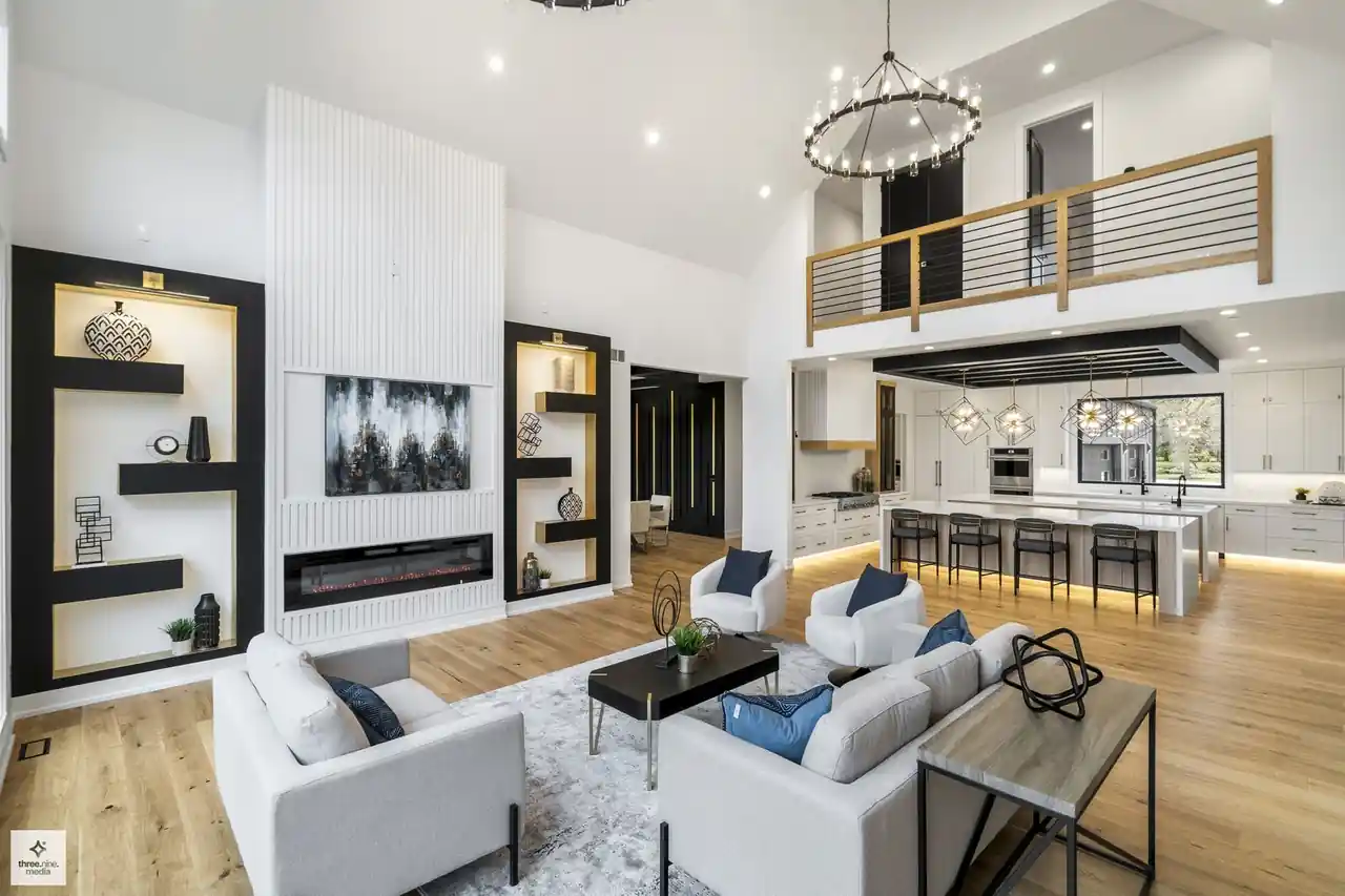 Living room seating area beneath a wood-railed loft overlooking the kitchen