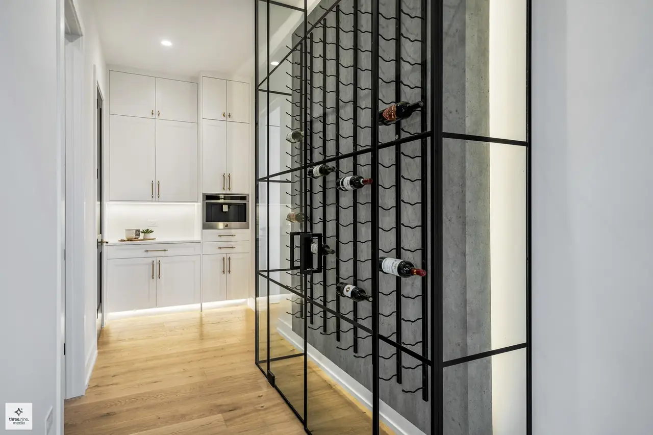 Glass-enclosed wine room with a wall-mounted bottle rack off the kitchen hallway