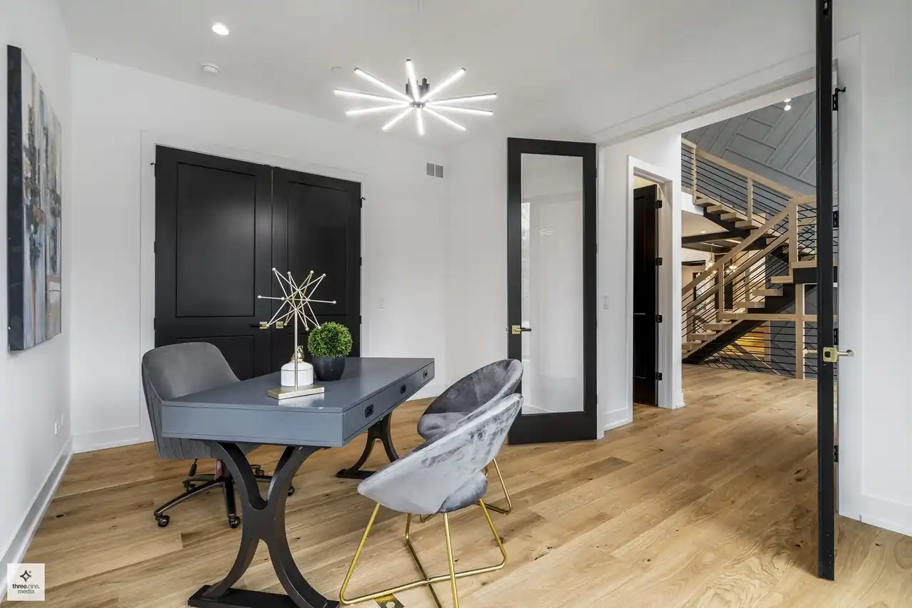Home office with black double doors, a starburst chandelier, and staircase view