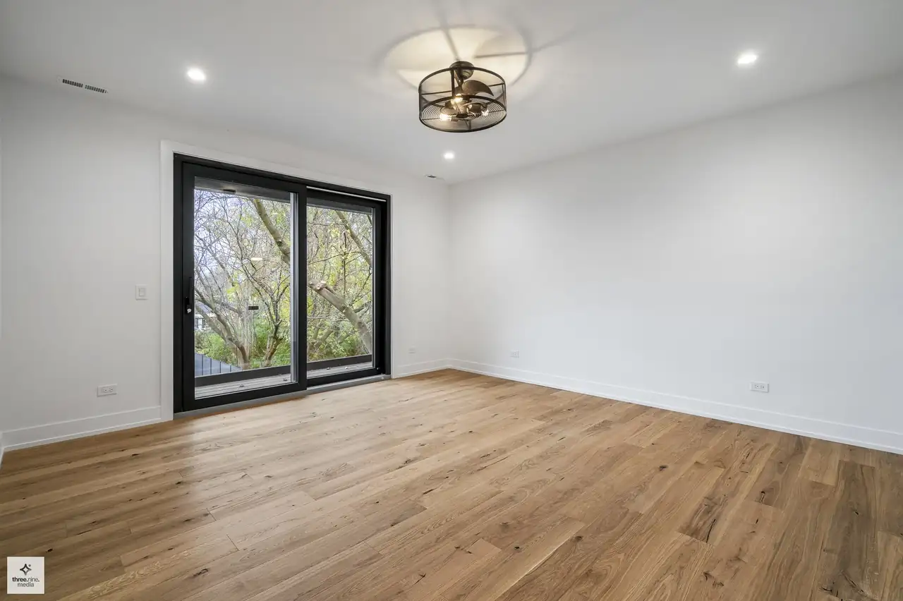 Unfurnished bedroom with a sliding glass door and tree-lined window view