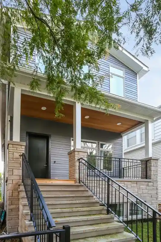 Exterior front porch of gray two-story new construction home with wood porch ceiling, stone columns, and staircase