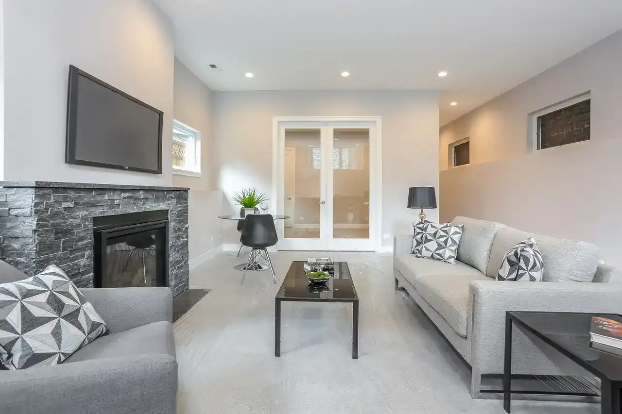 Basement family room with stone fireplace, wall-mounted TV, gray sectional sofas, and glass French doors